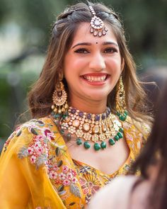 a smiling woman in a yellow sari with jewelry on her neck and headpiece