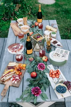 a picnic table with food and wine on it, including apples, blueberries, grapes, strawberries