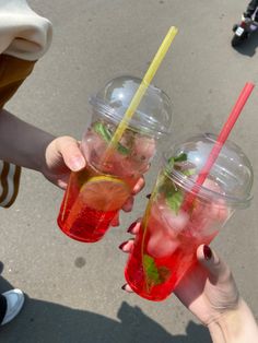 two people holding up drinks with strawberries and limes on them in their hands