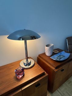 a table lamp sitting on top of a wooden dresser next to a bowl and plate