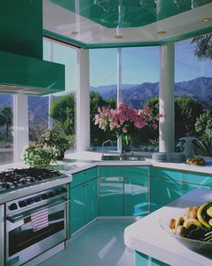 a kitchen with green cabinets and white counter tops is pictured in this image, there are pink flowers on the window sill