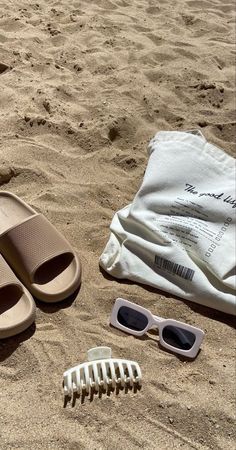 a pair of sandals, sunglasses and comb on the sand