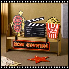 a movie clapper, popcorn box and other items on a wooden stand with the words now showing