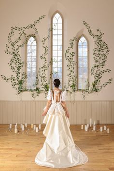 a woman in a wedding dress standing on a wooden floor with greenery behind her