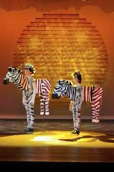 three children in zebra costumes standing on stage with their backs turned to the same direction