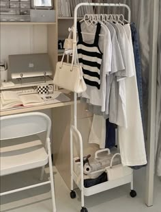 a white desk and chair with clothes hanging on the rack next to it in front of a laptop computer