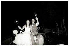 a man and woman sitting on top of a car holding sparklers