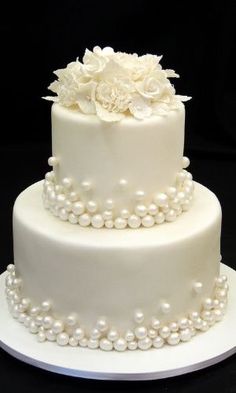 a three tiered wedding cake with white flowers and pearls