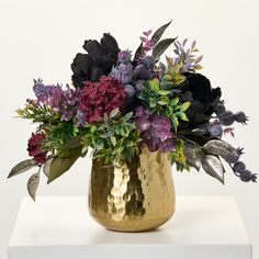 a gold vase filled with purple and black flowers on top of a white countertop