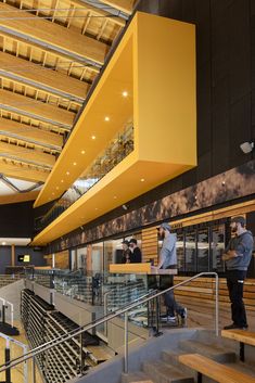 people are walking up and down the stairs in an open area with wooden benches, glass balconies, and metal railings