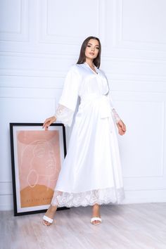 This white long robe is made of high-qualiry silk satin. It has long wide sleeves made of lace and wide belt. When you have one of the most important days in your life, everything should be perfect! You probably planned every minute of this day and now you are ready to make it real. The perfect day starts from the very morning which will be remembered every time you will look at your photos. The bride robe should be beautiful and comfortable at the same time so you could enjoy this day in full! White Robe With Lace Trim For Wedding Night, White Lace Trim Robe For Wedding Night, White Lace Trim Kimono For Wedding, Wedding White Kimono With Lace Trim, Satin Wedding Nightgown With Lace Trim, White Lace Trim Wedding Kimono, White Wedding Kimono With Lace Trim, Wedding Satin Nightgown With Lace Trim, Long White Robe For Home