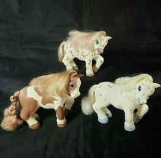 three small plastic horses on a black background with one horse in the foreground and another pony in the back ground