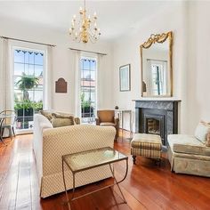 a living room filled with furniture and a fire place under a chandelier in front of two windows