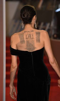 a woman with tattoos on her back walking down a red carpeted area in a black dress