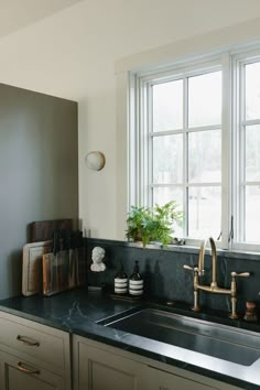 a kitchen sink under a large window next to a counter top with various items on it