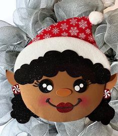 a close up of a wreath with a doll on it's face and wearing a santa hat