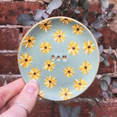 a hand holding a plate with yellow daisies on it, in front of a brick wall