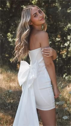 a woman wearing a white dress standing in the grass with her back to the camera