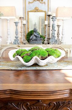 a wooden table topped with a white bowl filled with green moss next to two lamps