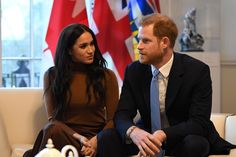 prince harry and his wife are sitting on a couch in front of flags