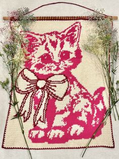 a cross - stitch cat with a bow on it's back and flowers in the background