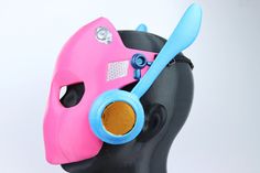 a pink and blue mask with a pair of scissors in it's mouth, on top of a black mannequin head