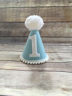 Please read shop announcement for current processing times and updates. Your birthday boy will look absolutely adorable in this mini birthday hat for his half birthday or whole birthday! Perfect for a party or photo shoot. The hat is available in 2 sizes, Mini which is 5 inches tall and 4 inches wide or Full size which is 7 inches tall by 5 inches wide. It features baby blue felt with a white number of your choice. White mini pom pom ribbon is attached along the base of the hat with a yarn Pom P Little Blue Truck Birthday Party, Blue Truck Birthday Party, Blue And White Party, First Birthday Hat, 1st Birthday Hats, Boys First Birthday Party, Little Blue Truck, First Birthday Hats, Boys First Birthday Party Ideas