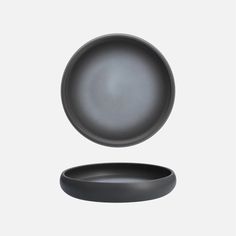 an empty black plate sitting on top of a white table next to a gray bowl