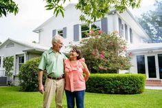 an older man and woman standing in front of a house