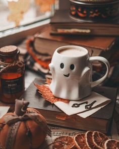 a coffee cup with a ghost face on it sitting next to some orange slices and books