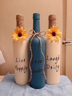 three bottles with words written on them and sunflowers tied to the top one