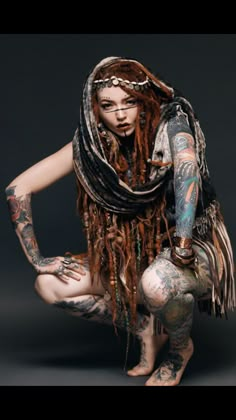 a tattooed woman kneeling down with her hands on her knees and arms wrapped around her body