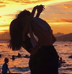 a woman standing on top of a sandy beach next to the ocean at sun set