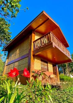 a wooden house sitting on top of a lush green hillside next to trees and flowers