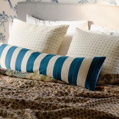 a bed with blue and white pillows on top of it next to a wallpapered headboard