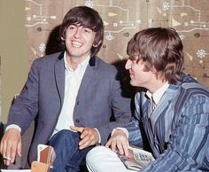 two young men sitting next to each other in front of a wallpapered background