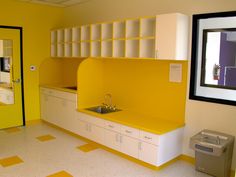 an empty kitchen with yellow and white walls, cabinets and counters in the center is a trash can