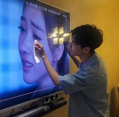 a man standing in front of a flat screen tv holding something up to his face