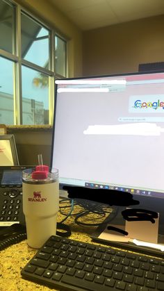 a computer monitor sitting on top of a desk next to a keyboard and mouse with a cup