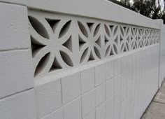 a white brick wall with an intricate design on the top and bottom part, along side a sidewalk