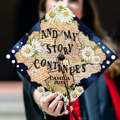 a woman holding a graduation cap that says and my story continues with daisies on it