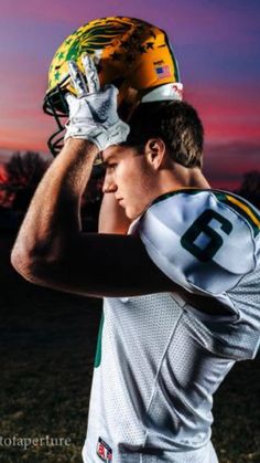 a football player is holding his helmet over his head and posing for the camera at sunset