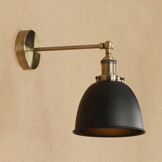 a wall light with a black shade hanging from it's side on a beige wall