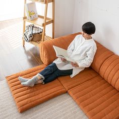 a woman sitting on an orange couch reading a book