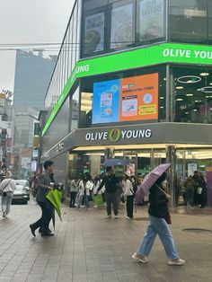 people walking on the sidewalk in front of an olive young store with green and white signs