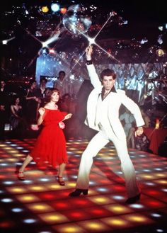 a man and woman dancing on a dance floor with disco lights in the back ground