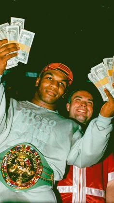 two men are holding up money in front of their faces and one is wearing a green belt