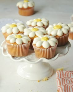 cupcakes with white frosting and yellow centers on a cake plate next to napkins