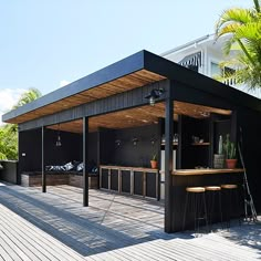 an outdoor bar with stools and tables on a deck next to palm trees in front of a house