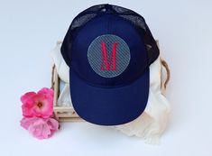 a blue hat with the letter m on it next to a pink flower